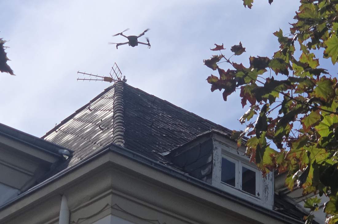 Drone en vol au-dessus d'un toit en ardoise, entre les branches d'un arbre
